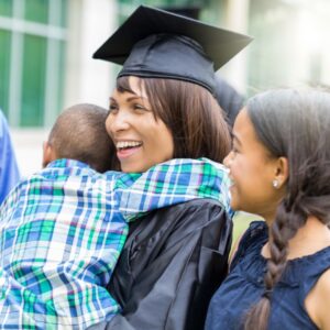 Woman in graduation cap and gown hugging her children